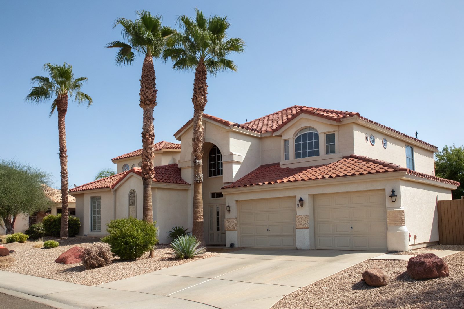 A two-story stucco home with a red concrete tile roof and palm trees