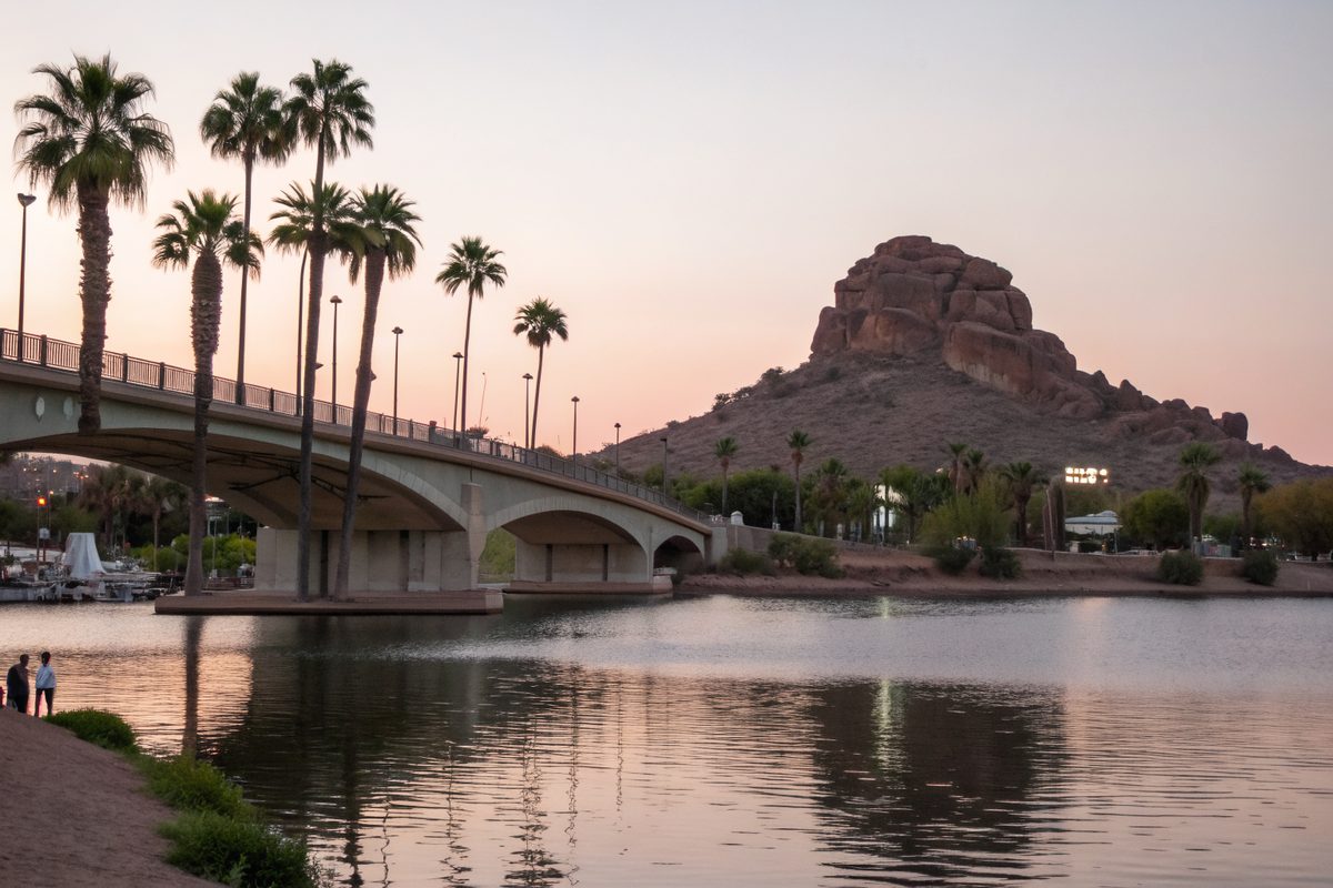 A calm urban lake with an arched bridge and a rocky butte at dusk